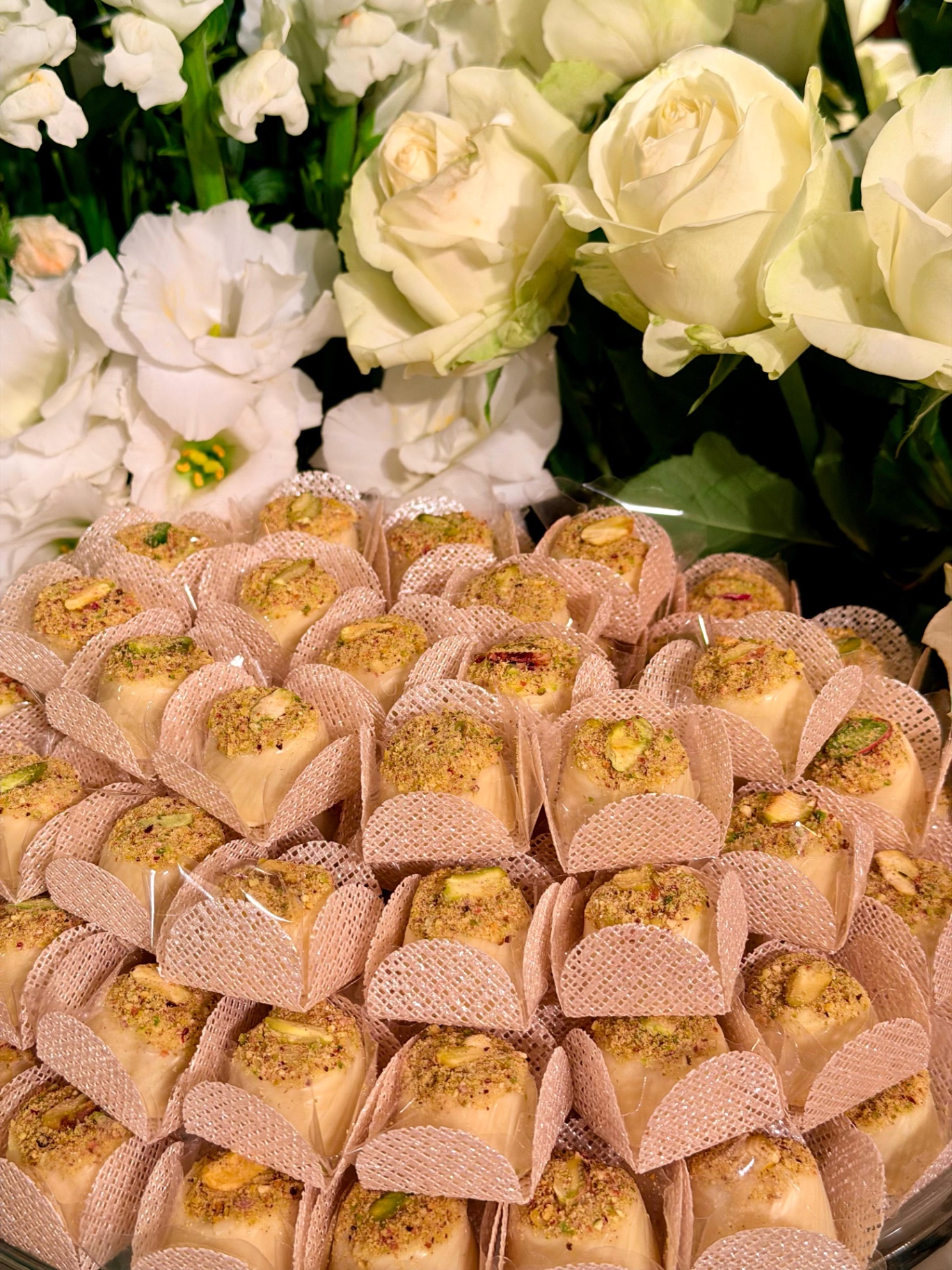 Bombons claros com pistache entre rosas brancas
