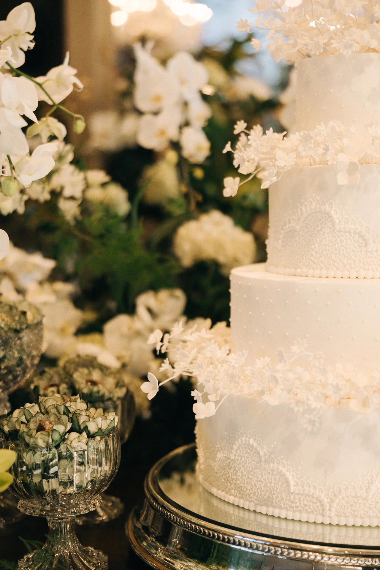 A white lace wedding cake nestled among orchid arrangements