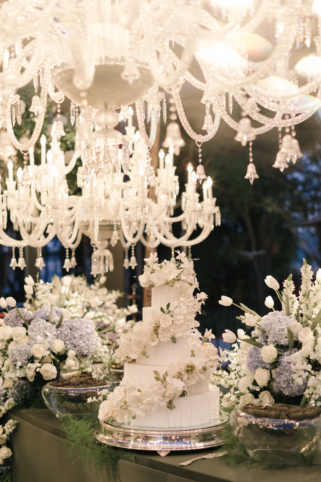 A wedding cake with white flowers beneath crystal chandeliers