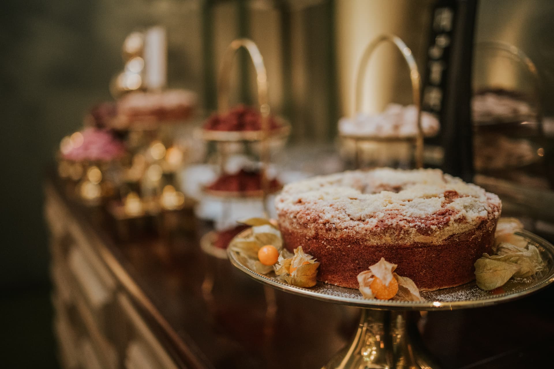 Bolo de corte em destaque sobre mesa de doces sofisticada, com petit-fours e doces finos ao fundo