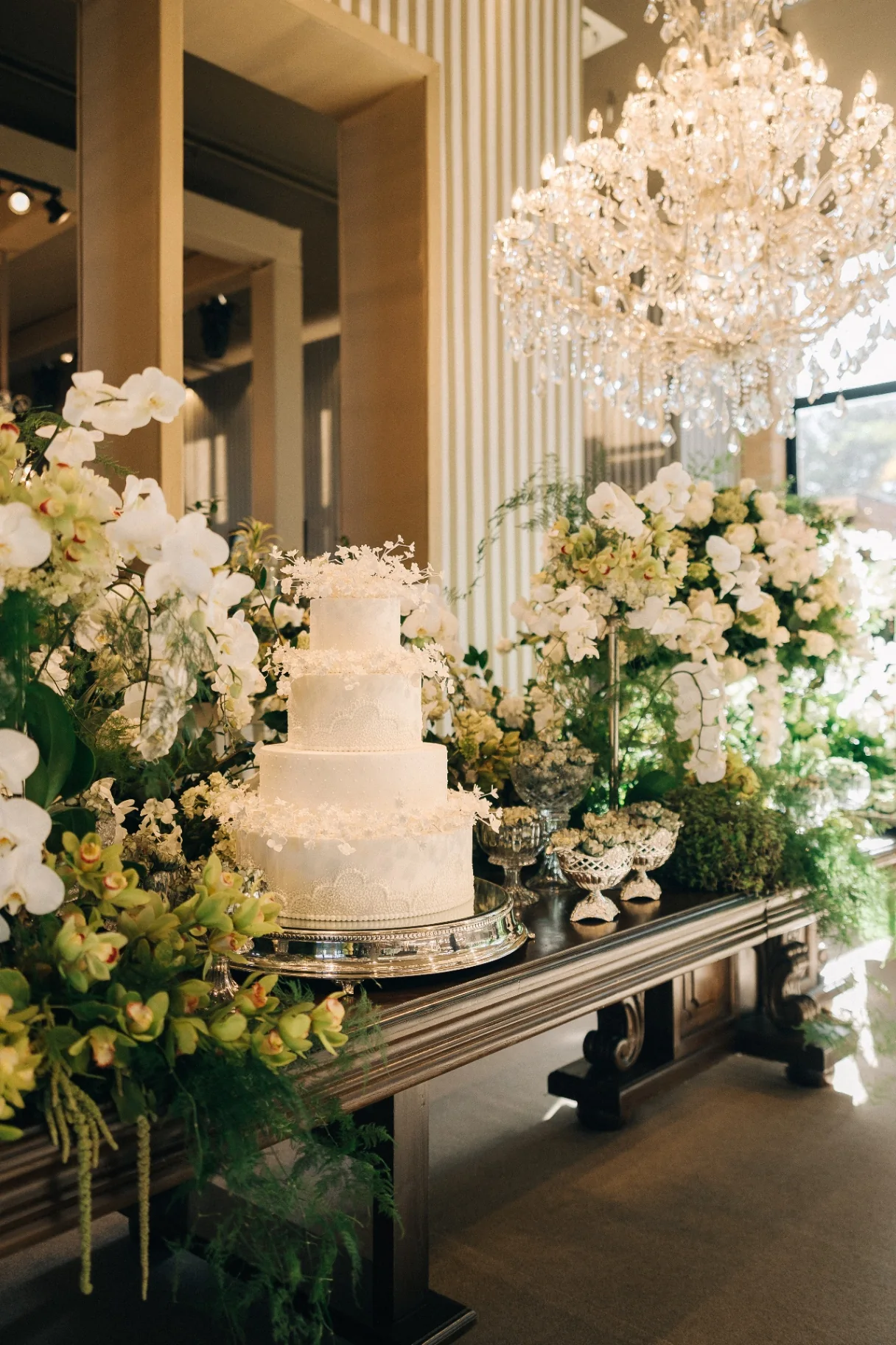 The cake table adorned with white flowers beneath a crystal chandelier