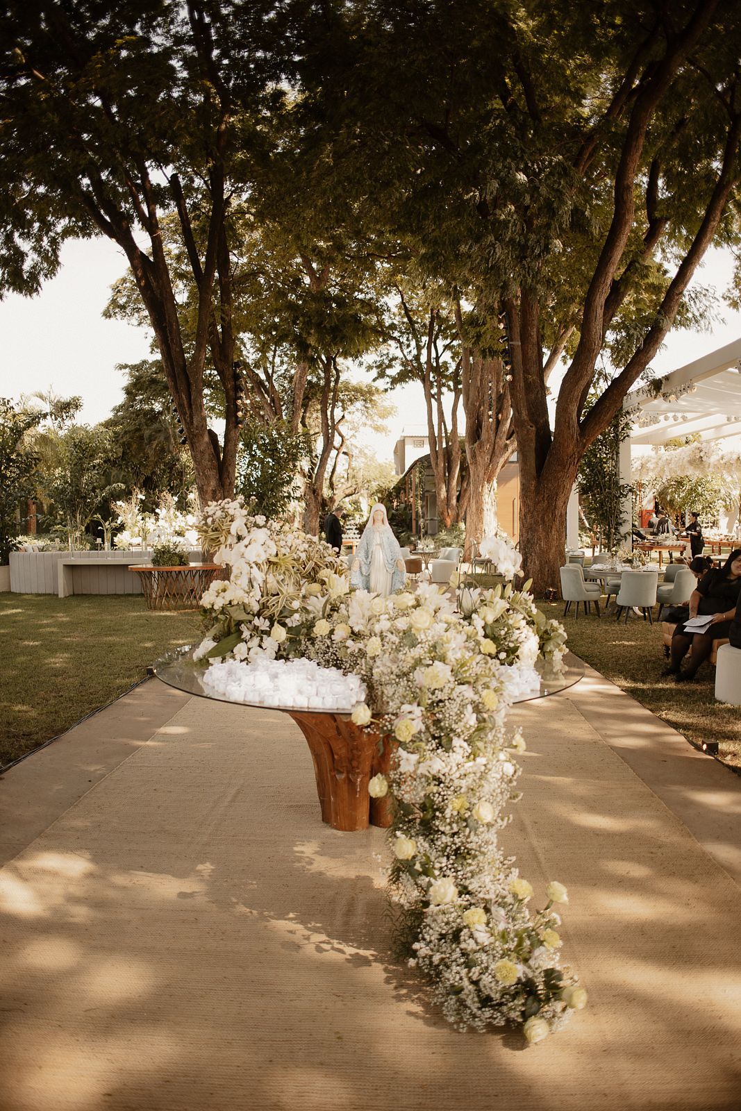 Mesa de doces ao ar livre com flores brancas e imagem de Nossa Senhora