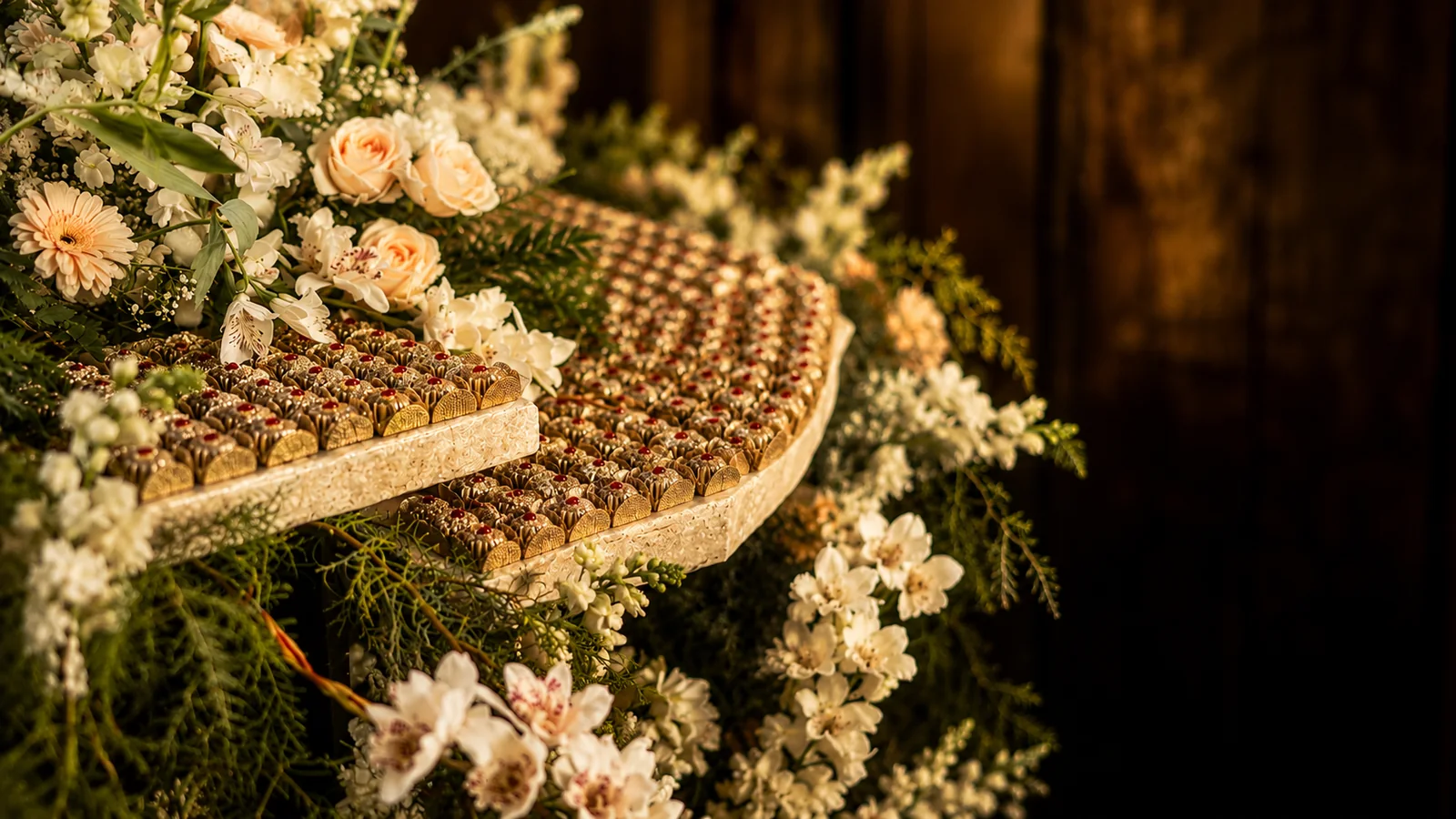 Mesa de doces de casamento ornada com flores e bombons dourados da Lebbeke
