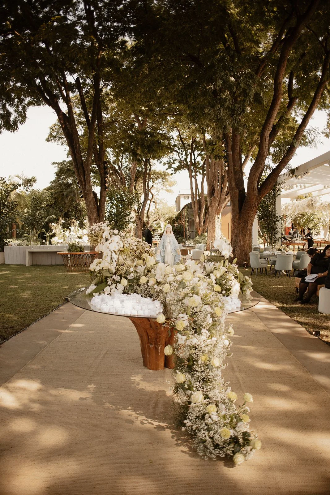 An outdoor dessert table with white flowers and a statue of Our Lady